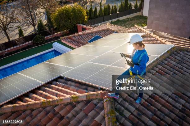 technikerin, die an der wartung von solar-photovoltaik-panel arbeitet, das auf dem heimischen dach mit einem tablet bei sonnenuntergang installiert ist - roofer stock-fotos und bilder