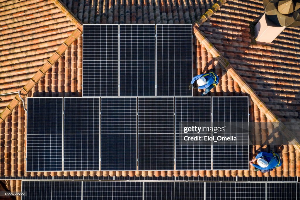 Vista aérea de dos trabajadores instalando paneles solares en una azotea