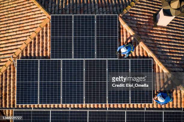 vue aérienne de deux travailleurs installant des panneaux solaires sur un toit - ceinture par dessus photos et images de collection
