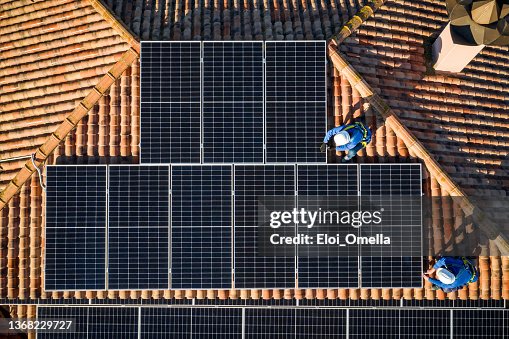 Aerial view of Two workers installing solar panels on a rooftop Aerial view of Two workers installing solar panels on a rooftop