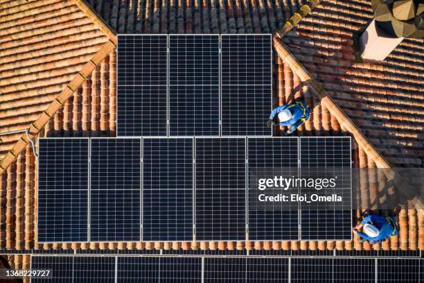 aerial view of two workers installing solar panels on a rooftop - tile roof stock pictures, royalty-free photos & images