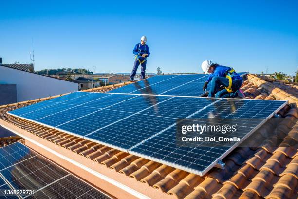 männliche und weibliche arbeiter, die sonnenkollektoren auf einem dach installieren - house roof materials stock-fotos und bilder