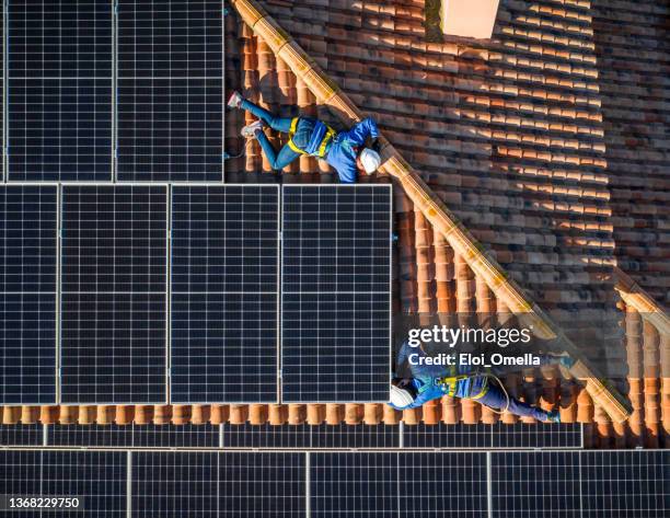 two professional worker installing solar panels lying down on the roof of a house. aerial view - safety harness stockfoto's en -beelden