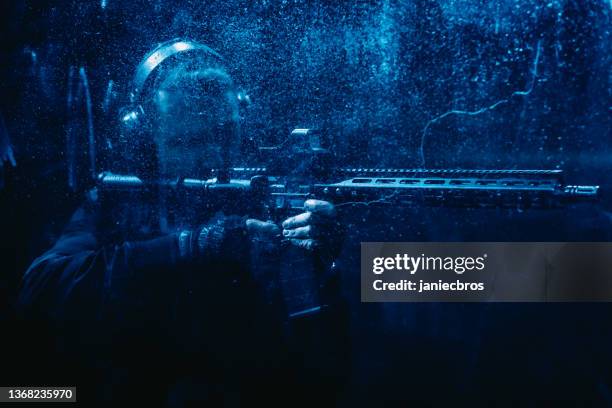 man aimimg m4 ar-15 rifle in dark, foggy shooting range. splashing droplets, blue light - gunman 個照片及圖片檔