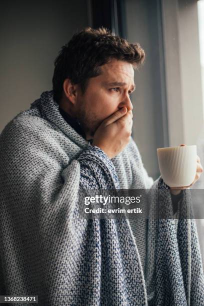 sick man with blanket coughing , trying to get better with drinking hot beverage - covid 19 symptoms stock pictures, royalty-free photos & images