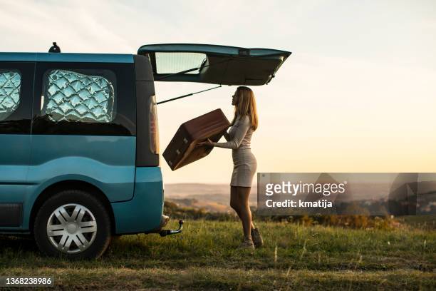 young woman loading suitcase in trunk of a camper van in rural scene - white van profile stock pictures, royalty-free photos & images