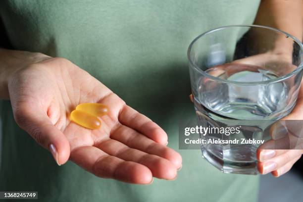 the woman is holding omega-3 fish oil capsules or medications, and a glass of water. healthy lifestyle, prevention and treatment of diseases. the girl takes and drinks food supplements and vitamins. biologically active additive. intake of healthy fats. - cod liver oil stock pictures, royalty-free photos & images