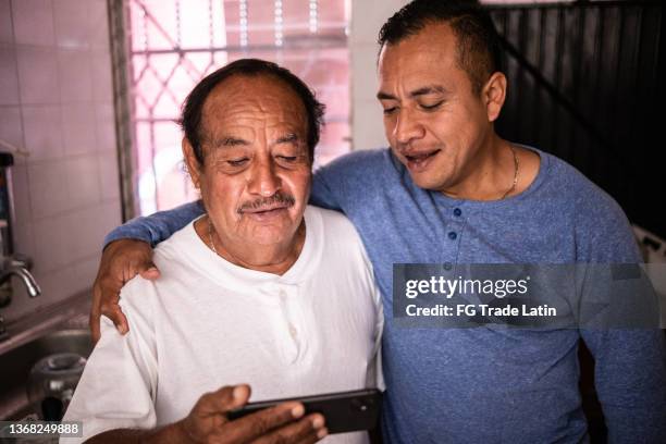 latin father and son using the mobile phone at home - mexico nuit stock pictures, royalty-free photos & images