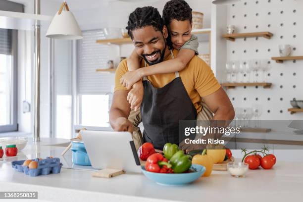 un jeune garçon s’amuse avec son père tout en préparant un repas sain - tablier photos et images de collection