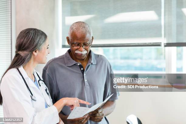 senior man looks at brochure as doctor explains options presented - male doctor man patient stockfoto's en -beelden