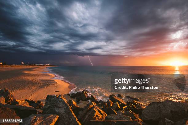 incredible beach sunset during lightning storm beneath dark dramatic clouds - overcast beach stock pictures, royalty-free photos & images