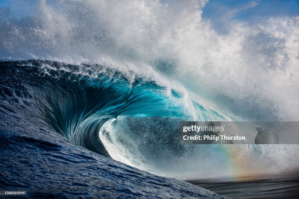 Potente onda oceanica che si infrange con un accenno di arcobaleno che brilla attraverso