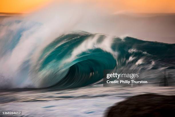 powerful crashing turquoise wave in front of golden sky - surf tube stock pictures, royalty-free photos & images