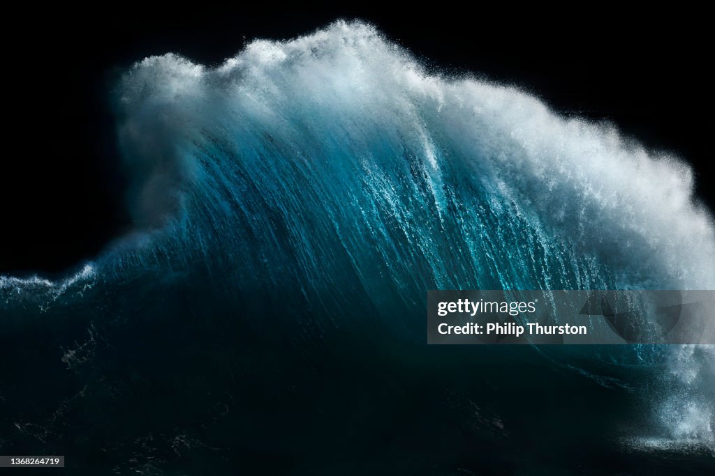Powerful ocean wave exploding into the air in front of dark sky