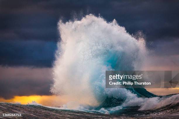 powerful wave exploding into sky during multi colored sunset - explosive imagens e fotografias de stock