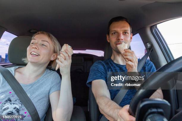 young happy couple eating ice cream, laughing and enjoying driving car while traveling. road trip date with ice cream cone dessert - eating in car stock pictures, royalty-free photos & images