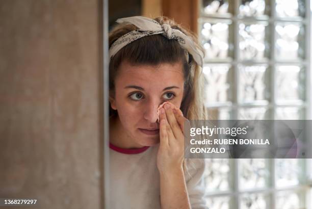 young caucasian teenager removing facial treatment in front of a mirror. healthcare and medicine concept. - abschminken stock-fotos und bilder