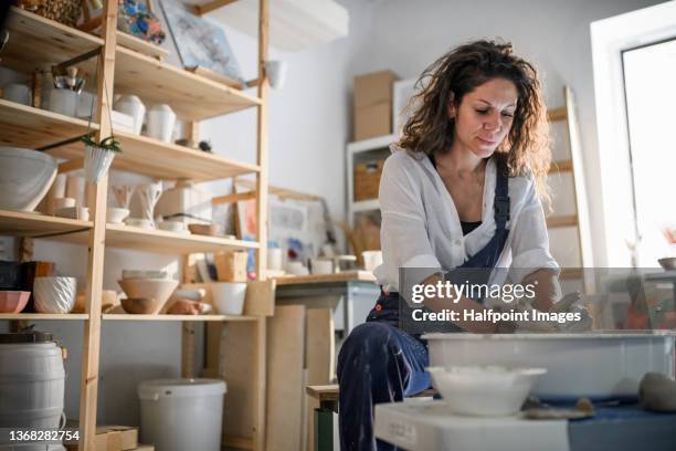 low angle view of mid adult woman, making pottery on a pottery wheel in art studio. - pottery wheel stock pictures, royalty-free photos & images