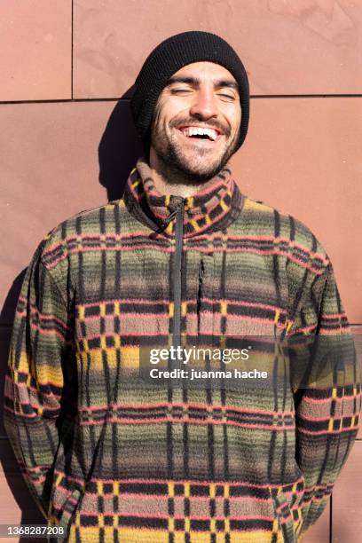 bearded man in sweater smiling in front of the camera under the sun. - hipster man stock pictures, royalty-free photos & images