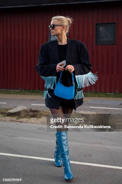 Guest wearing black jacket with blue tassel, blue long boots and blue bag outside Soulland in Copenhagen fashion week Autumn/Winter 2022 on February...