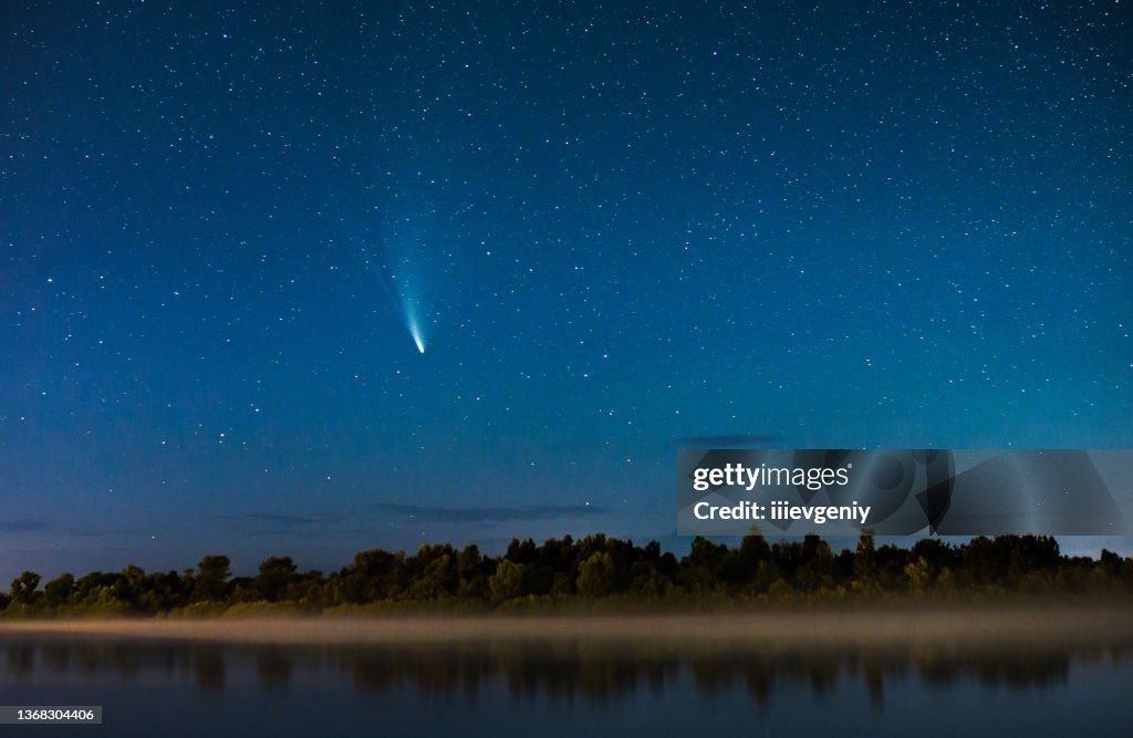 Comet in the night sky. Summer starry sky. Stars on sky. Beautiful night landscape. Long exposure. Conceptual photography. Fog over the water. Atmospheric landscape. Morning twilight. Comet Neowise