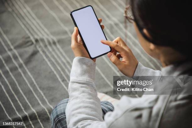 over the shoulder view of asian woman using phone in her bedroom - over the shoulder view stock pictures, royalty-free photos & images