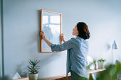 Young Asian woman decorating and putting up a picture frame on the wall at home