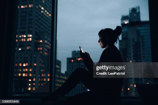 woman sitting by a window in manhattan - smart cities stockfoto's en -beelden