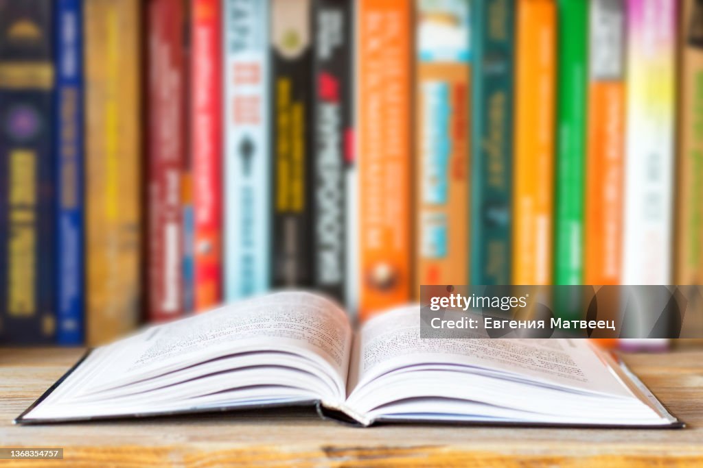 Close-up of opened book on bookshelf on blurred books background. Home library reading books concept