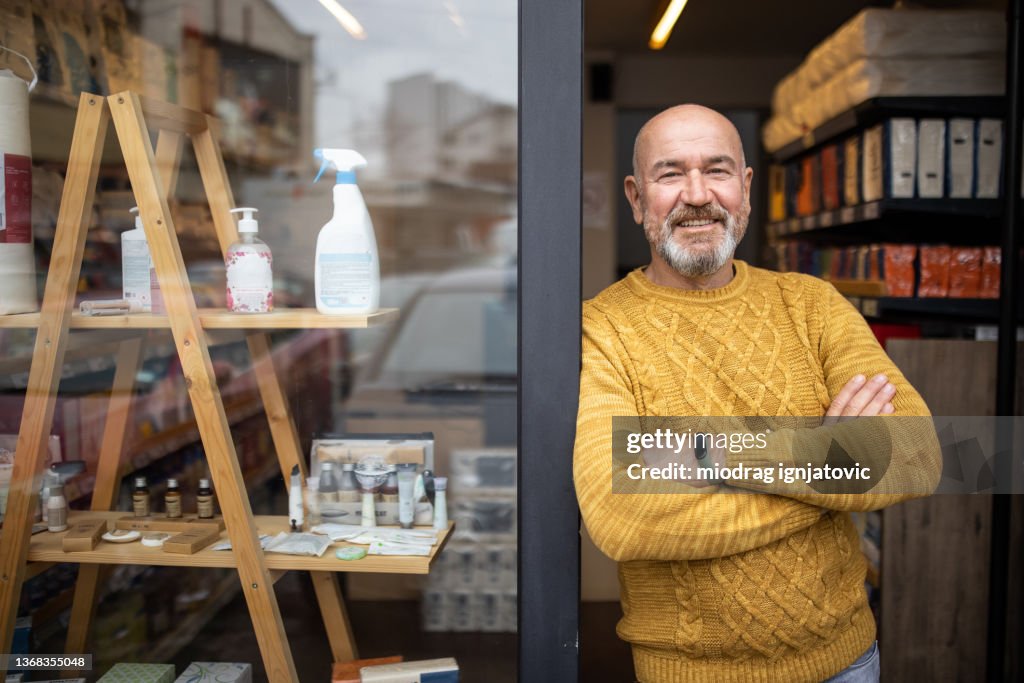 Proud owner standing with arms crossed in front of his store