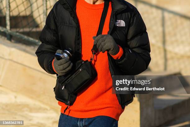 Passerby wears a black puffer jacket from The North Face, a neon orange embossed checkered pattern pullover, gray wool gloves, a black fanny pack...