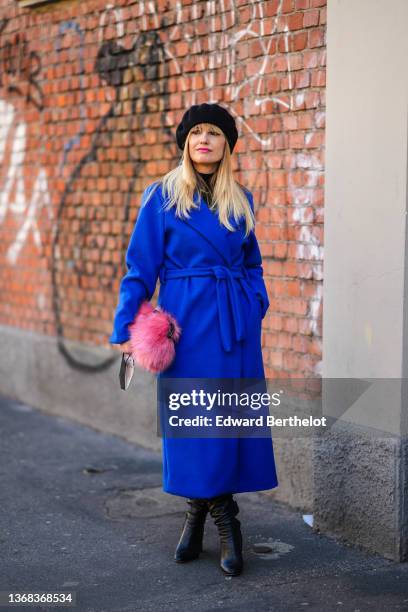 Guest wears a black felt beret, a black turtleneck pullover, a royal blue electric belted long coat, black shiny leather pointed heels knees boots, a...