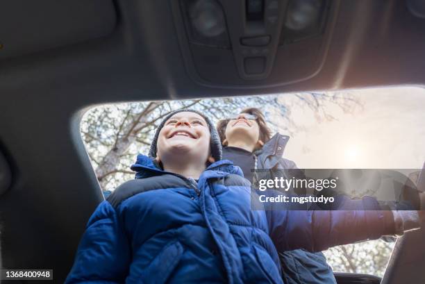 happy brothers enjoying freedom on sunroof of car in autumn. - sunroof stock pictures, royalty-free photos & images