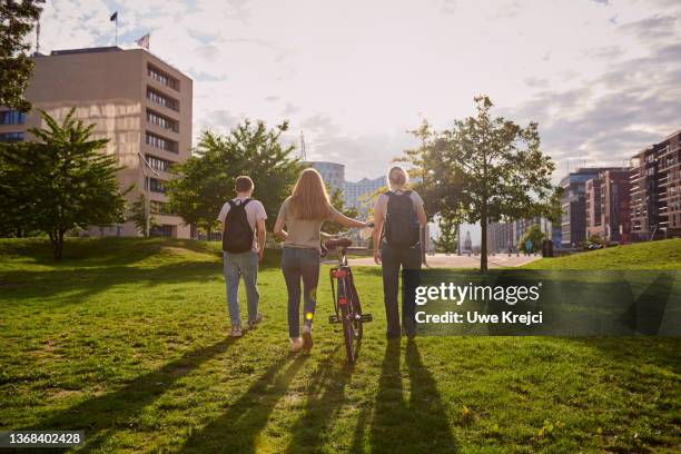 rear view of friends walking through public park - young white people walking stock-fotos und bilder