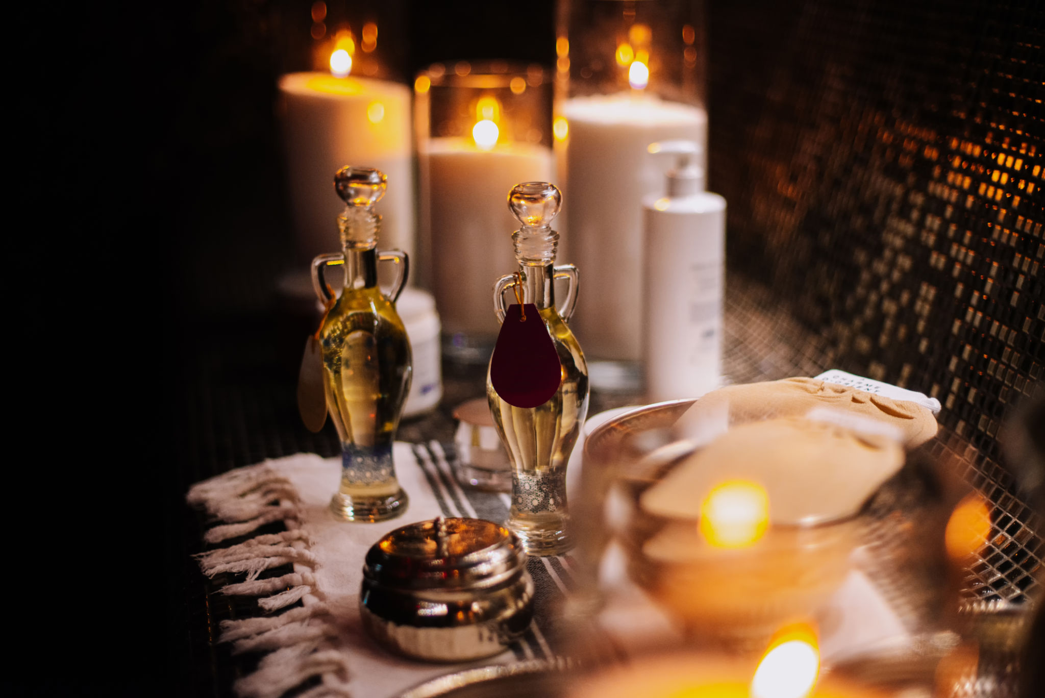 Essential oils with various herbs and flowers near candles Essential oils with various herbs and flowers near candles