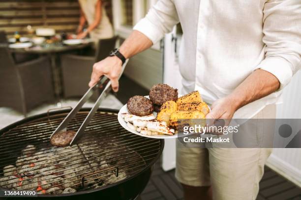midsection of mature man preparing barbecue meal in back yard - backyard grilling stock-fotos und bilder
