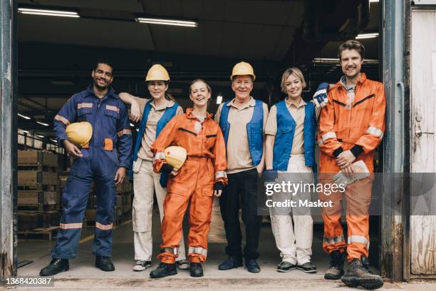 portrait of smiling male and female workers in workwear at entrance of warehouse - 作業員 ストックフォトと画像