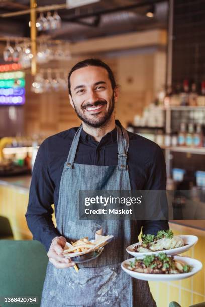 portrait of smiling male waiter with food in restaurant - ober stockfoto's en -beelden