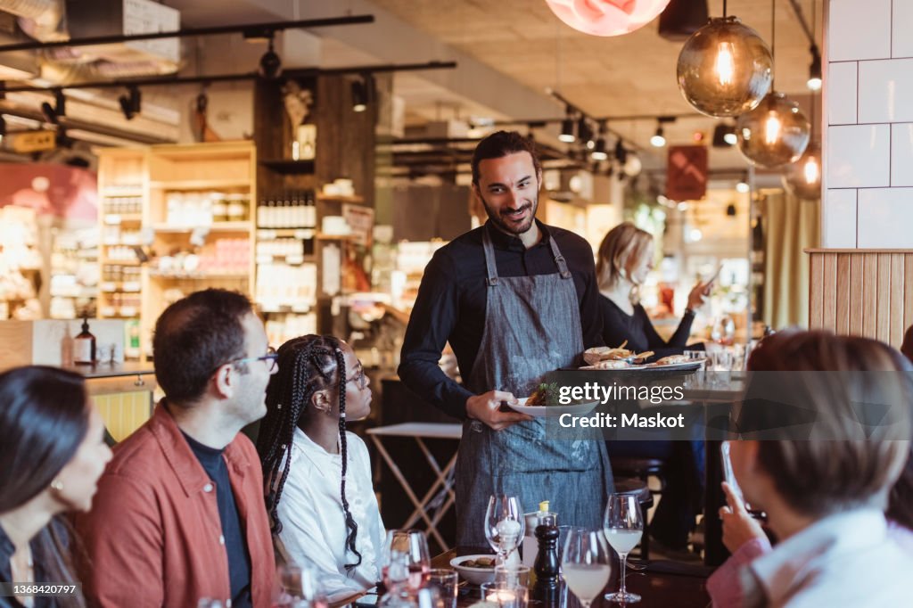 Waiter serving food to multiracial customers during party in restaurant