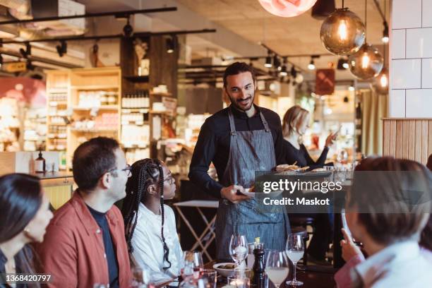 waiter serving food to multiracial customers during party in restaurant - camarero fotografías e imágenes de stock