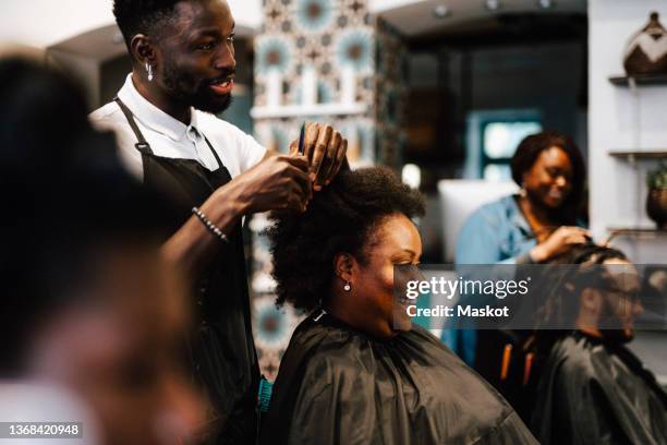 male hairdresser cutting hair of smiling female customer at barber shop - hairdressers black woman stockfoto's en -beelden