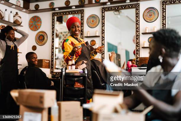happy female barber talking with male coworker while working in salon - hairdressers black woman stockfoto's en -beelden