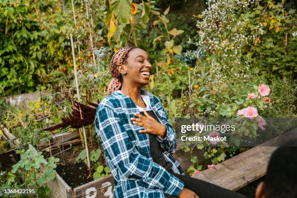cheerful young woman laughing while sitting in urban farm - main sur la poitrine photos et images de collection