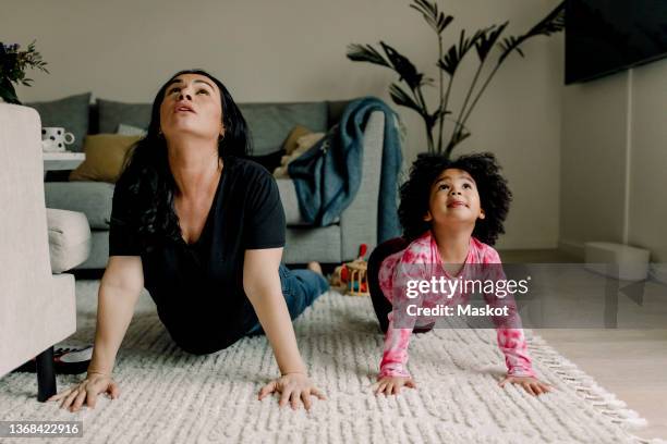 mother and daughter practicing yoga in living room at home - home workout stockfoto's en -beelden