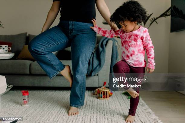 low section of mother teaching tree pose to daughter at home - op een been staan stockfoto's en -beelden