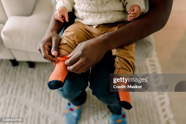 high angle view of father putting on sock to son in living room at home - getting dressed stock pictures, royalty-free photos & images