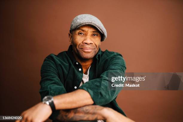 portrait of mature man wearing beret over brown background in studio - smiling people color background stock pictures, royalty-free photos & images