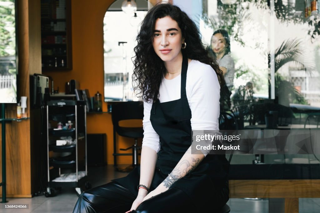 Portrait of female owner sitting against hair salon
