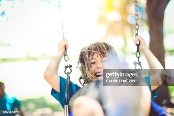 cute laughing elementary age girl enjoys being pushed on a swing outdoors by a classmate on a playground - school yard stock pictures, royalty-free photos & images