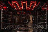 Looking inside the black empty kitchen oven. There is a lattice shelf and a red hot heating element. Background.